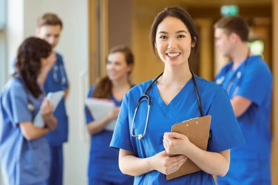 Licensed Practical Nurse Smiling with Clipboard in Front of RNs