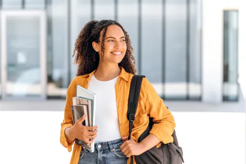 Student wearing backpack and smiling holding textbook