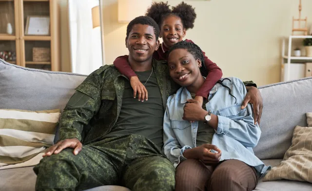 Portrait of African American family of three smiling at camera sitting on sofa with their military dad
